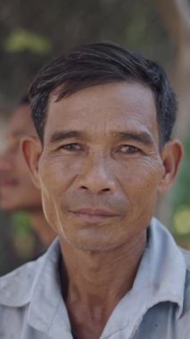 Vietnam 'daki FullHD dikey kameraya bakan, çok sucai tişörtlü ve saçında kamış olan olgun bir Asyalının portresi.