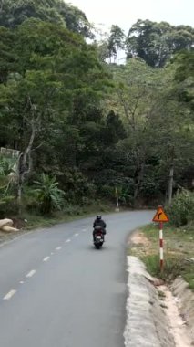 Vietnam ormanları arasında kırsal ve sessiz bir alanda dar virajlı bir yol boyunca motosiklet takip eden insansız hava aracı