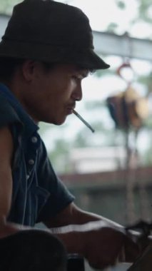 Genç Asyalı tamirci Vietnam 'da ağzına sigara tıkıştırılmış penseyle kazıcı küreğine vuruyor.