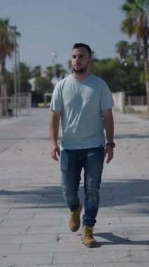 Palmiye ağaçları arasındaki beton yol boyunca kameraya bakan beyaz çocuk akıllı telefonundan yapılan bir çağrıya cevap verdi.