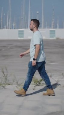 Palmiye ağaçları arasındaki çimento geçidi boyunca kameraya doğru yürüyen beyaz çocuk akıllı telefonuyla bir ses notu gönderiyor.