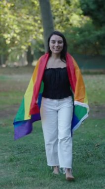 Genç beyaz kız çimenlerin üzerinde çıplak ayakla yürüyordu kameradan yüzünü çevirmişti arkasında bir LGBT bayrağı vardı FullHD dikey