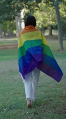 Genç beyaz kız çimenlerin üzerinde çıplak ayakla yürüyordu kameradan yüzünü çevirmişti arkasında bir LGBT bayrağı vardı FullHD dikey