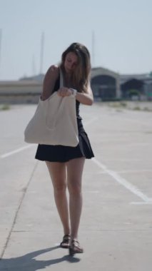 Beyaz kısa siyah elbiseli genç bir kız limanın yakınındaki sanayi bölgesinde kameraya doğru yürüyor. Tek koluyla taşıdığı büyük çantasında asılı duran bir şeyi arıyor.