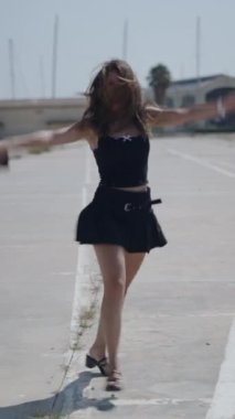 Kafkasyalı kısa siyah elbiseli genç bir kız kameraya bakarken mutlu ve memnun bir şekilde müzik dinliyor ve kulaklıklarında kulaklıklarla dans ediyor.