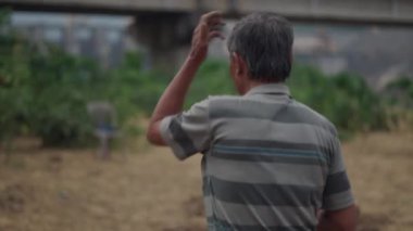 Kamera yetişkin bir Vietnamlı erkek çiftçinin adımlarını takip ediyor. Bahçedeki çalışma gününde. 4K Yatay.