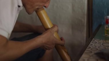 Olgun Asyalı adam Vietnam 'da bir bardaktan içerken büyük el yapımı ahşap bir pipodan tütün yakıyor - 4K Yatay