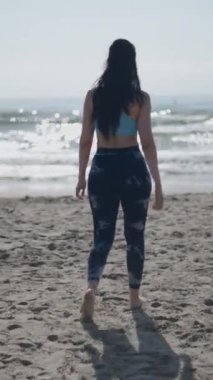 Uzun saçlı esmer, at kuyruklu beyaz bir kadın güneşli bir günde kumsaldaki kumsalda kameraya doğru yürüyordu.