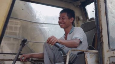 Vietnam 'da kameraya gülümseyen yaşlı bir vinci kontrol eden Asyalı genç bir çocuğun portresi - 4K Yatay
