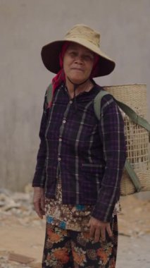 Zavallı ve mütevazı Vietnamlı olgun bir kadın sırtında sepetle kameraya bakıyor.