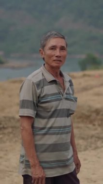 Nehir ve doğa yakınlarındaki kırsal bir alanda kameraya bakıp gülümseyen Vietnamlı çiftçinin portresi.