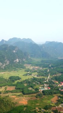 Büyük kayalık dağlarla çevrili ovadaki köy ve Vietnam 'da birçok bitki örtüsü - FullHD dikey video