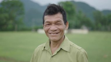 Vietnam 'da yüzünde kırışıklıklar olan, gülümseyen ve kameraya el sallayan olgun bir Asyalı çiftçinin portresi - 4K Yatay