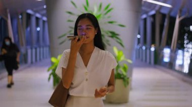 Asyalı bir kız caddeden karşıya geçerken kameraya doğru yürüyor. Akıllı telefonuyla bir sesli mesaj gönderiyor. 4K Yatay.