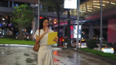 Asyalı kız gece Bangkok gezinti alanında kameraya doğru yürürken tabletle video görüşmesi yapıyor - 4K Yatay