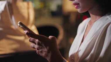 Beyaz ipek bluzlu genç kadın ekranına dokunarak akıllı telefonuyla etkileşime giriyor - 4K Yatay