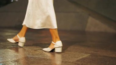 Sırtı dönük genç bir kadının bacakları ve beyaz ayakkabıları geceleyin caddede yürüyordu - 4K Yatay