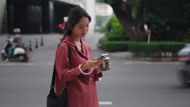 Genç Asyalı kadın akıllı telefon kullanıyor ve şehir caddesinde kahve içiyor - 4K Yatay