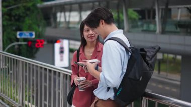 Genç Asyalı çift kahve paylaşıyor ve şehir köprüsünde akıllı telefon kullanıyor - 4K Yatay