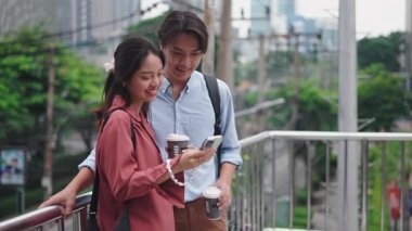 Genç Asyalı çift akıllı telefon kullanıyor ve açık havada kahve içiyor - 4K Yatay