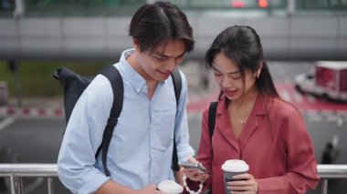 Genç Asyalı çift köprüde akıllı telefon kullanıyor ve kahve içiyor - 4K Yatay