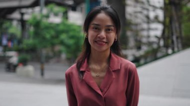 Kentsel ortamda gülümseyen ve göz kırpan genç Asyalı iş kadını - 4K Yatay