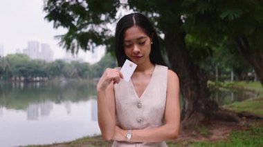 Genç Asyalı iş kadını kredi kartı alışverişini internette yapıyor. Parkta dizüstü bilgisayar kullanıyor. 4K Yatay