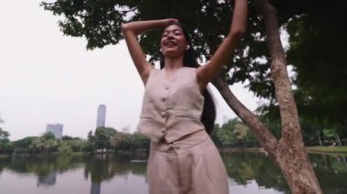 Göl kenarındaki bir parkta günlük kıyafetlerle dans eden ve kulaklıklarıyla müzik dinleyen genç bir kadın.