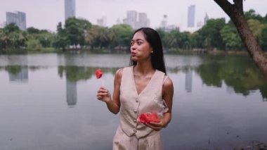 Güzel genç bir kadın, şehir parkındaki bir gölün yanında taze karpuz yiyor - 4K Yatay