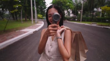 Genç bir kadın taşınabilir yelpazesinden gelen ferahlatıcı esintinin keyfini çıkarırken alışveriş torbaları taşıyor - 4K Yatay