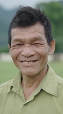 Vietnam 'da kameraya gülümseyen ve el sallayan yüzü buruşuk Asyalı olgun bir çiftçinin portresi.