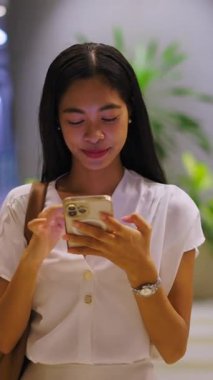 Asyalı bir kız, Bangkok 'ta elinde akıllı telefonuyla caddeden karşıya geçerken kameraya gülüyor.