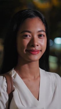 Kameralar, geceleri Bangkok 'ta ayakta duran beyaz elbiseli Asyalı genç kadının yüzüne zumluyor.