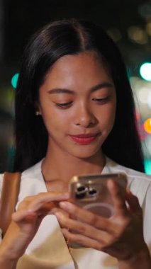 Akşamları akıllı telefonunun ekranına dokunurken kameraya gülümseyen genç bir kadının yüzü ve elleri.