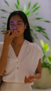 Asyalı bir kız caddeden karşıya geçerken kameraya doğru yürüyor akıllı telefonuyla sesli mesaj gönderiyor FullHD Dikey