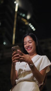 Esmer Asyalı kız, Bangkok 'taki tren raylarının yanındaki büyük şehirde gece video görüşmesi yapıyor.