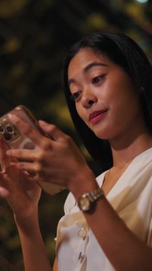 Asyalı esmer kız, bir yaz gecesi bileğinde saatle akıllı telefon ekranına dokunuyor.