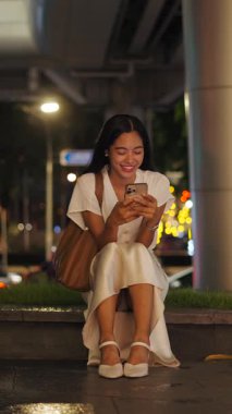 Beyaz elbiseli Asyalı kız ve köprü altında oturan ayakkabılar akıllı telefonuyla bir şeyler yolluyor.