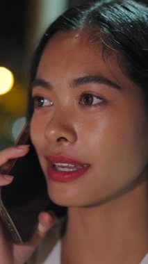 Tayland 'da yağmurlu bir gecede sokakta telefonla konuşan Asyalı bir kızın yüzüne yakın çekim - FullHD Dikey
