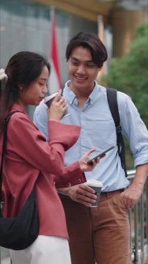 Genç Asyalı çift, şehir yaya köprüsünde kahve içip akıllı telefon kullanıyor.