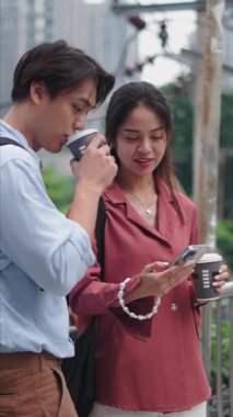 Akıllı telefon kullanan ve kahve içen genç Asyalı çift FullHD Dikey