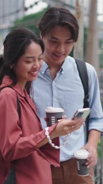 Akıllı telefon kullanan ve dışarıda kahve içen genç Asyalı çift FullHD Dikey