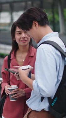 Genç Asyalı çift kahve paylaşıyor ve şehir köprüsünde akıllı telefon kullanıyor - FullHD Dikey