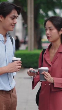 Genç Asyalı turistler akıllı telefonlarıyla geziyorlar ve şehir caddesinde kahve içiyorlar.