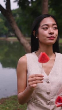 Huzurlu park ortamında bir çubukta taze karpuzun tadını çıkaran kadın - FullHD Dikey