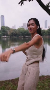 Kulaklık takan kaygısız genç kadın, Lumpini Park 'ta bir gölün kenarında dans ediyor.