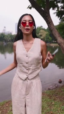 Kalp şeklinde güneş gözlüğü takan genç bir kadın parkta dans ediyor ve müzik dinliyor.