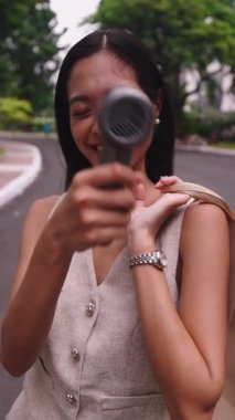 Genç bir kadın, portatif yelpazesinden gelen ferahlatıcı esintinin keyfini çıkarırken alışveriş poşetleri taşıyor.