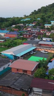 Tayland 'ın kırsal kesiminde ağaçlar ve yol arasında inşa edilmiş küçük evleri olan insansız hava aracı manzaralı bir köy.