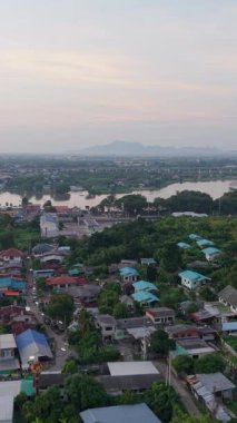 Tayland 'da yolun yanındaki kırsal alanda bulunan göl kenarındaki evlerin havadan görünüşü FullHD Dikey